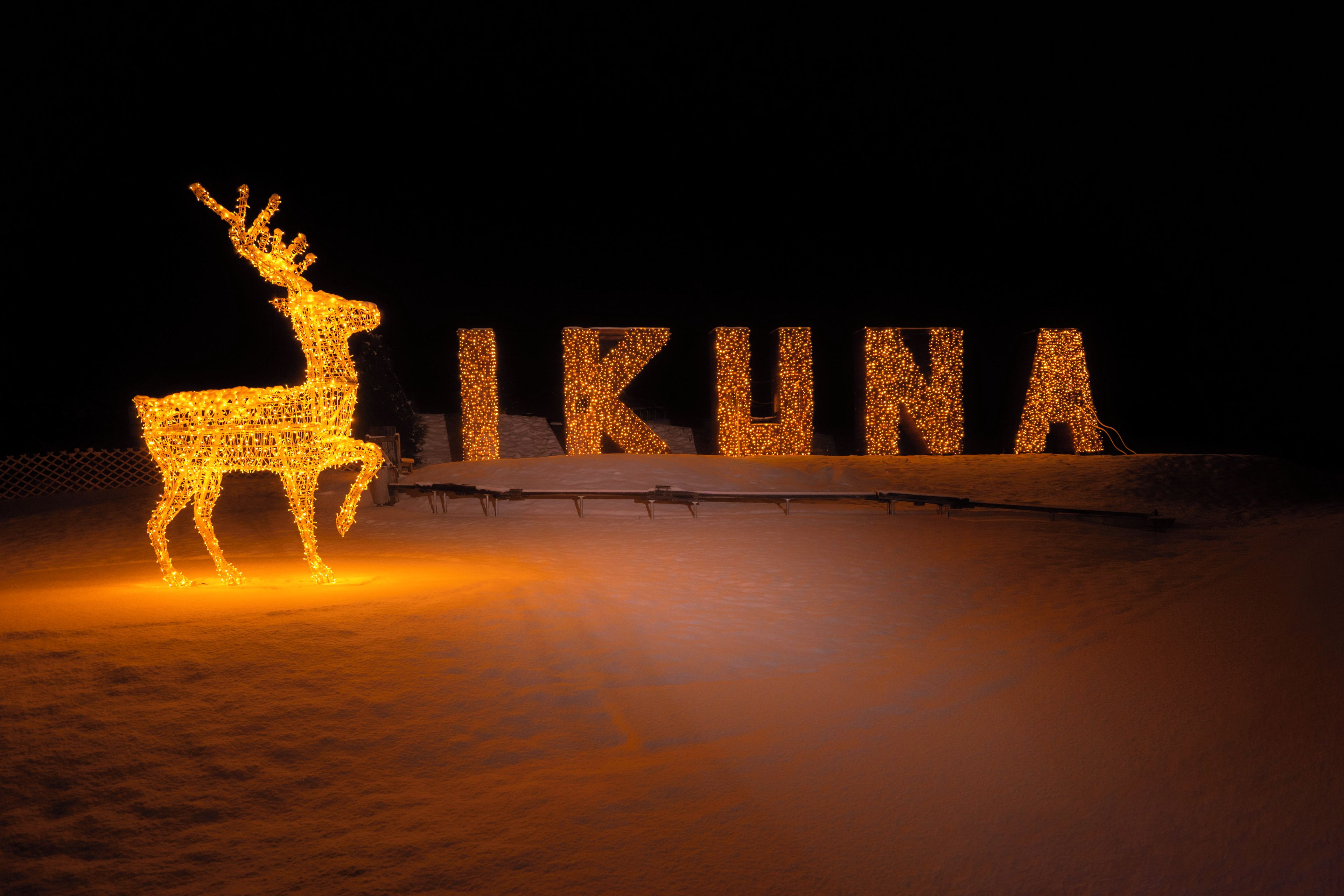 A deer silhouette and illuminated letters spelling 'IRUNA' on a snowy surface at night.