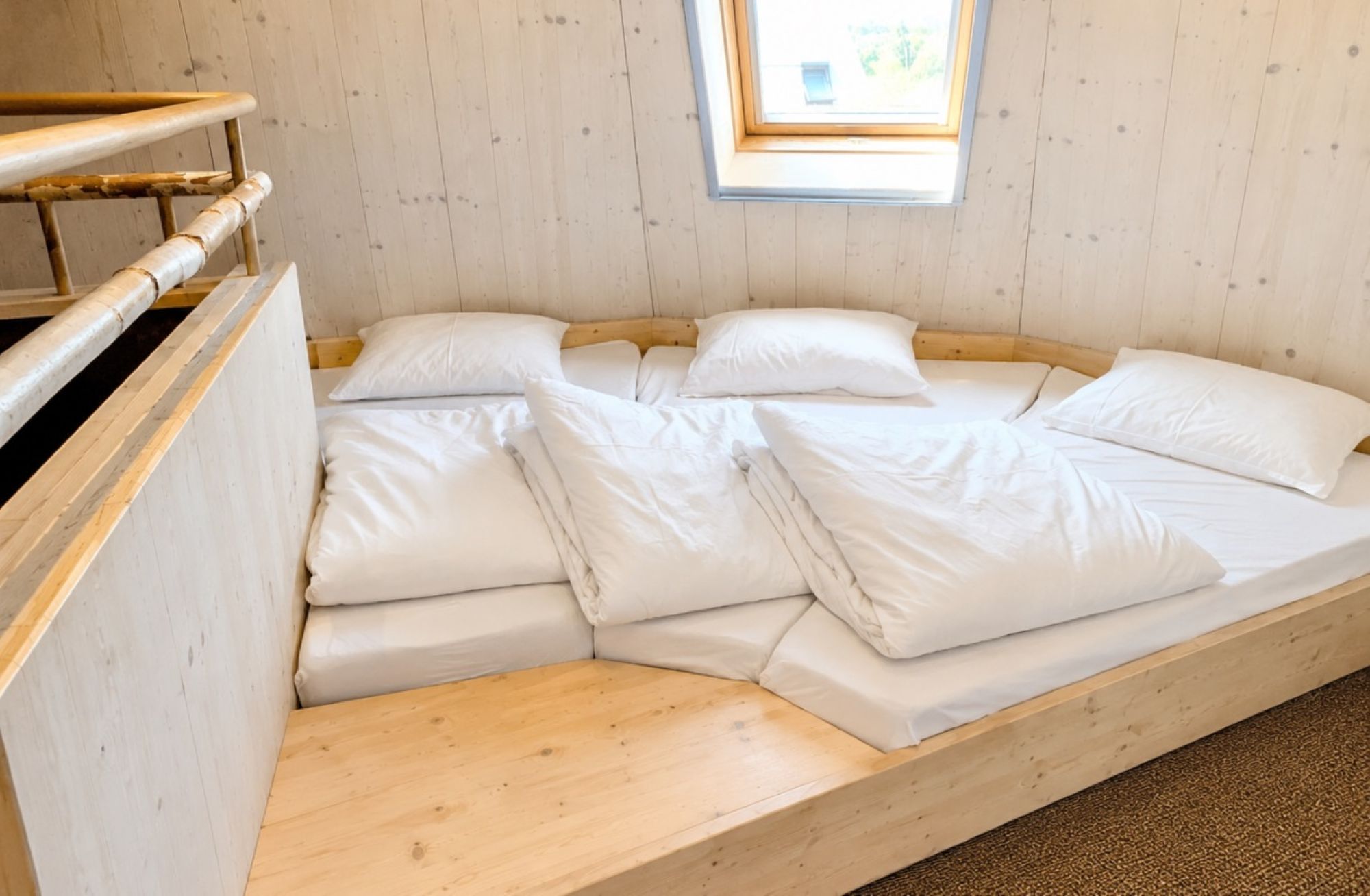 A wooden bunk bed with white bedding, a small skylight, and a wooden headboard.