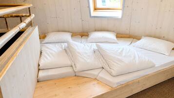 A wooden bunk bed with white bedding, a small skylight, and a wooden headboard.