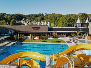 A swimming pool with water slides, a spa & pool building, and a landscaped area with trees and umbrellas. - Ikuna Naturresort (Natternbach)