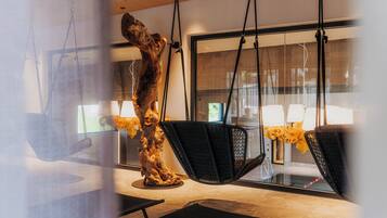 Ein modernes Interieur mit einem großen Fenster, einer hängenden Holzskulptur und schwarzen Stühlen mit strukturierter Oberfläche.