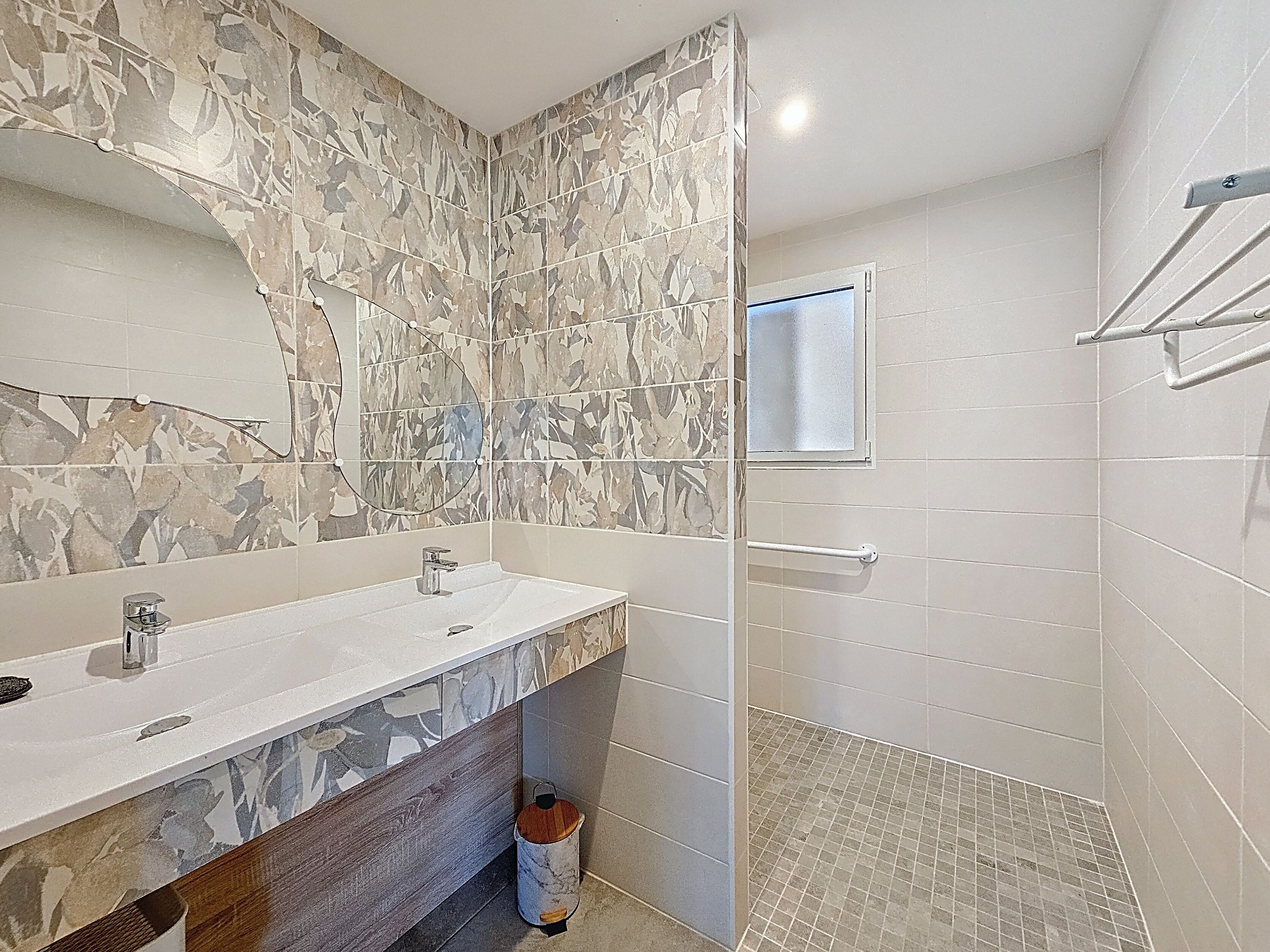A bathroom with a marble vanity, a mirror, a shower with a glass door, and a towel rack.