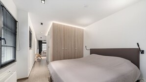 Een moderne slaapkamer met een groot bed, een inbouwkast en een hal die naar een andere kamer leidt.