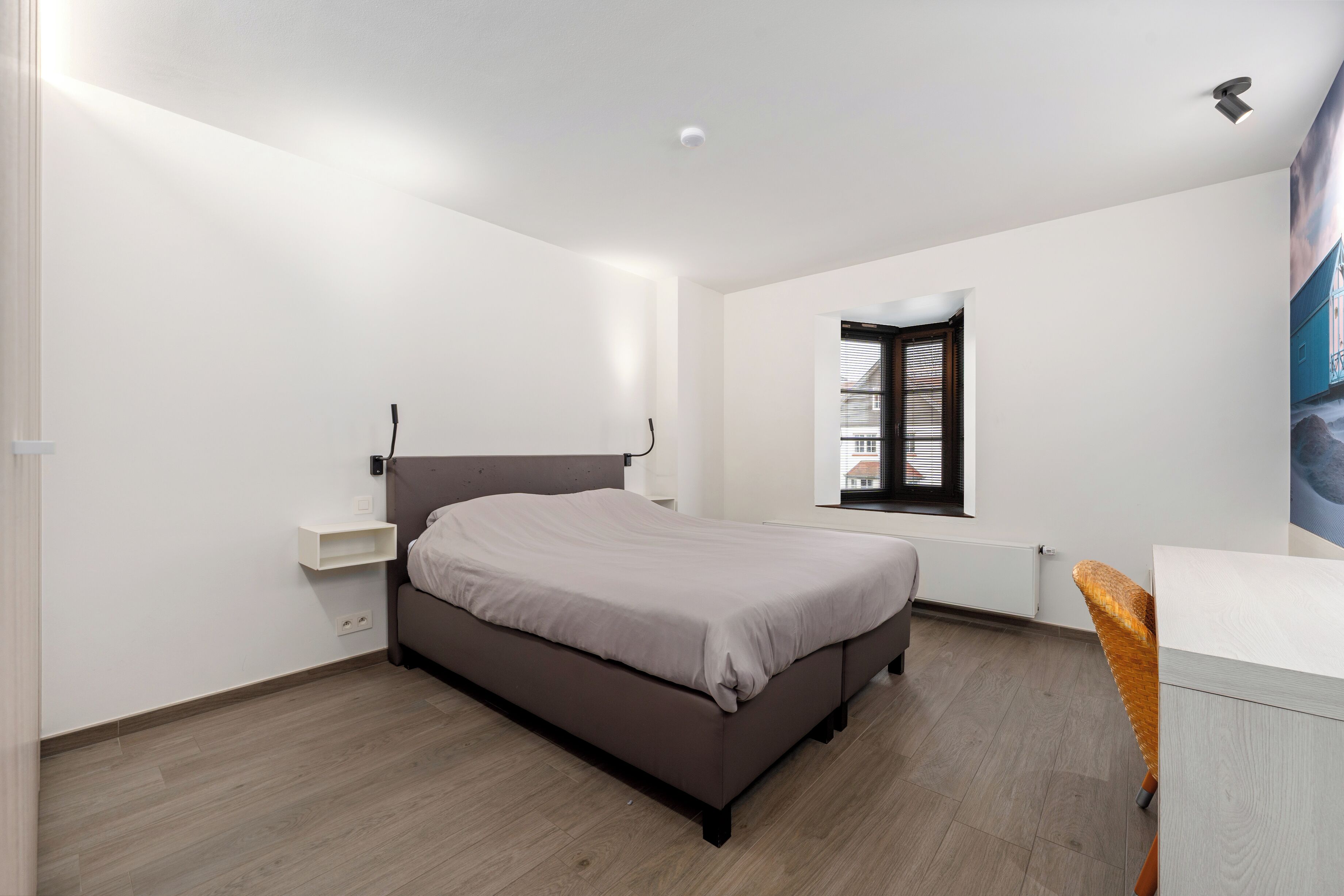 Un dormitorio con cama, escritorio, silla, ventana y radiador.