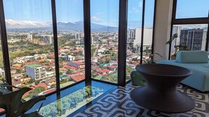 Habitación en un edificio alto con ventanales que ofrecen vistas a la ciudad, una mesa redonda moderna y un suelo estampado.
