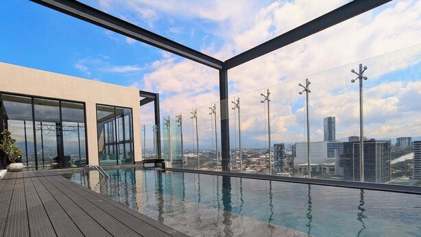Una piscina infinita en la azotea con terraza de madera, ventanas amplias y vista panorámica de la ciudad.
