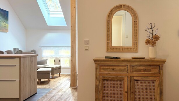 Een kamer met een houten dressoir, een spiegel en een vaas met bloemen.