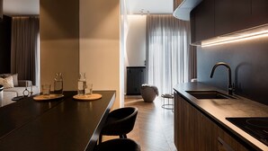 A modern kitchen with a dark countertop, a built-in sink, and a sleek faucet. There is a bar area with stools and a small table with glassware. - Bullet Athens (Athina)