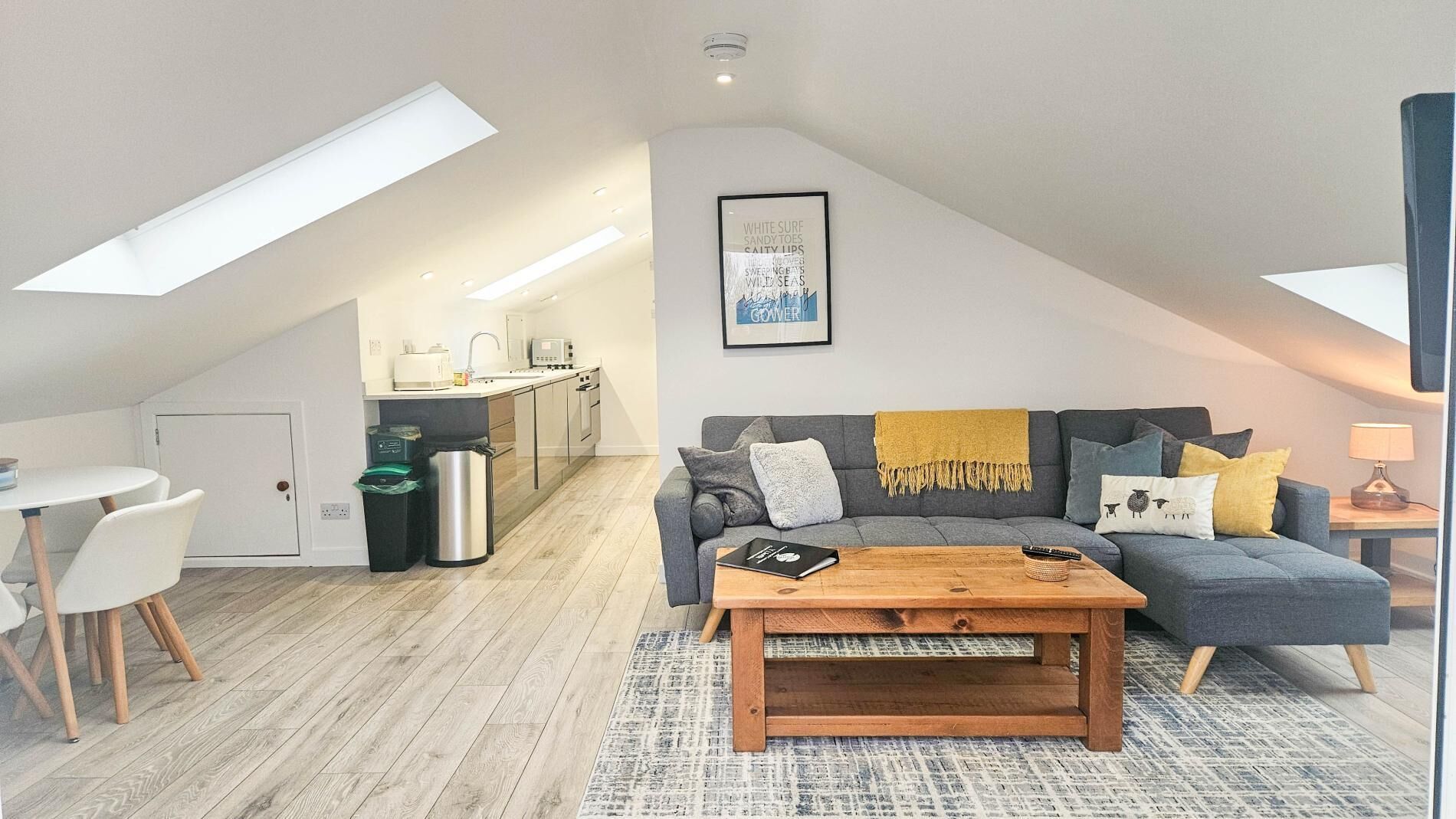Moderni loft-tyylinen huoneisto, jossa on ruokailutila, pieni keittiö sekä viihtyisä olohuone, jossa on sohva ja sohvapöytä.