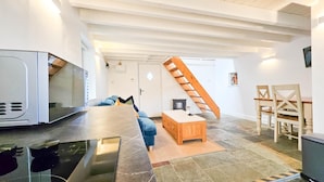 A modern living room with a large flat-screen TV, a wooden coffee table, a sofa, and a staircase. - Y Stabl - 1 Bedroom Apartment - Llanrhidian (Swansea)