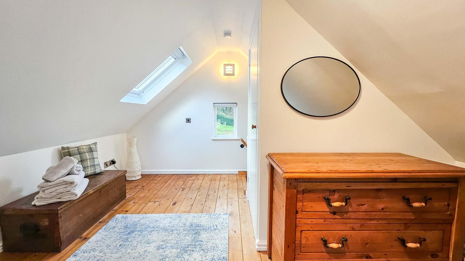 A room with a sloped ceiling, a skylight, a wooden dresser, a bench with towels, and a mirror on the wall.