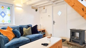 A cozy living room with a blue sofa, a white coffee table, and a black wood-burning stove. - Y Stabl - 1 Bedroom Apartment - Llanrhidian (Swansea)