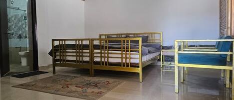 Une chambre avec un lit en bois, une petite table et une chaise, et une salle de bain visible à travers une porte en verre.