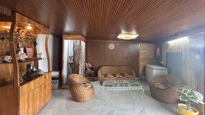 A cozy living room with wooden paneling, a wicker sofa, a metal coffee table, and a potted plant. - The Chail Heights Hotel & Resort (Shimla)