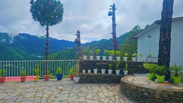 A stone-paved terrace with potted plants, a stone wall, and a view of mountains. - The Chail Heights Hotel & Resort (Shimla)