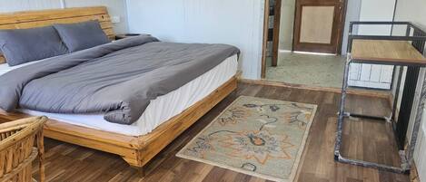 A single bed with a wooden frame, grey bedding, and a patterned rug.