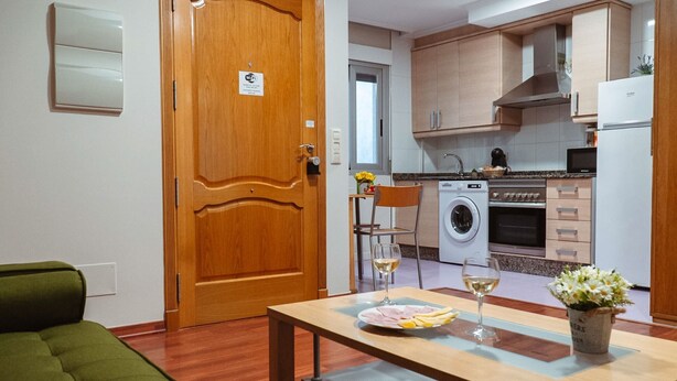 Een moderne keuken met houten kastjes, een wasmachine en een eethoek met een tafel gedekt voor twee personen.