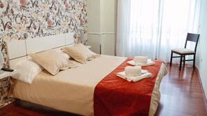 Een netjes opgemaakt bed met een rode deken, witte kussens en een opgevouwen handdoek aan de zijkant.