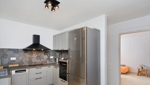 A modern kitchen with grey cabinets, a stainless steel refrigerator, a built-in oven, and a hexagonal tile backsplash. - Serenity Near the Sea (Gaios)