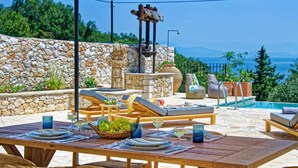 An outdoor dining area with stone walls, a pool, and lounge chairs. - Serenity Near the Sea (Gaios)