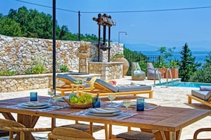 An outdoor dining area with stone walls, a pool, and lounge chairs.