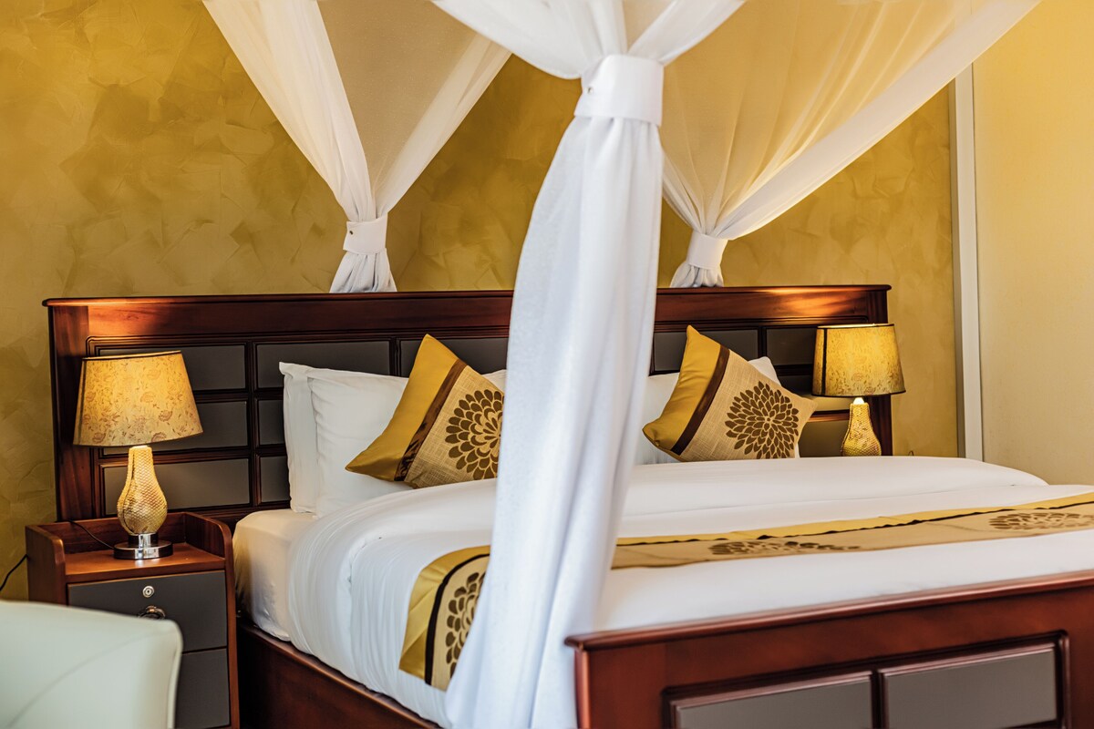 A four-poster bed with a canopy, two bedside lamps, and decorative pillows.