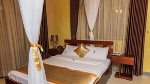 A hotel room with a bed, curtains, a nightstand, and a lamp. - Nican Resort Hotel (Kampala)