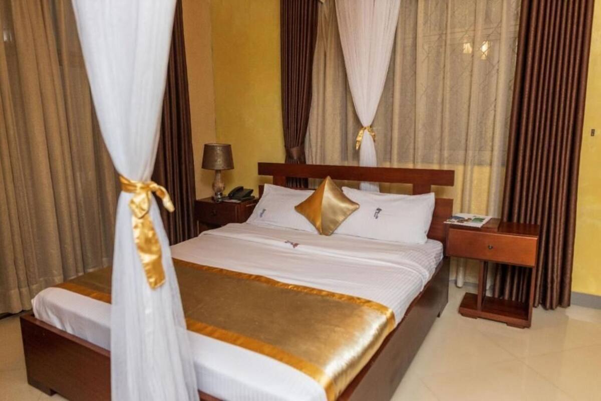 A hotel room with a bed, curtains, a nightstand, and a lamp.