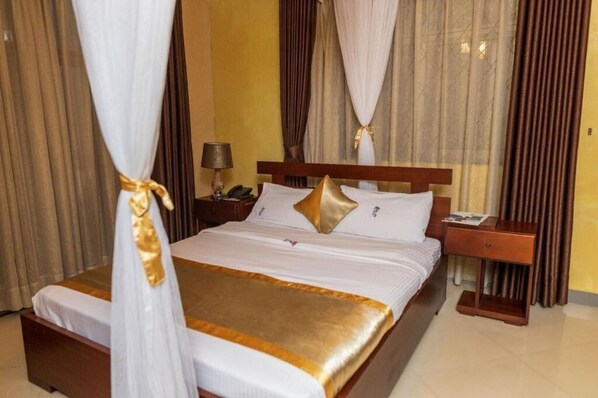 A hotel room with a bed, curtains, a nightstand, and a lamp. - Nican Resort Hotel (Kampala)