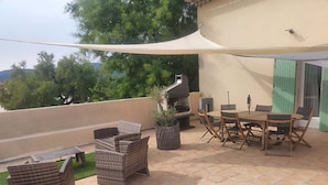 An outdoor patio with wicker furniture, a barbecue grill, and a table with chairs.