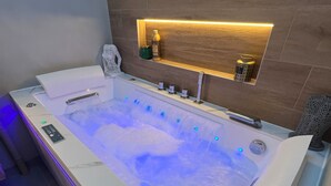 A modern bathroom with a large bathtub, wooden wall paneling, and a shelf with toiletries.