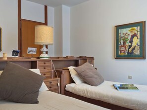 Een hotelkamer met twee bedden, een houten dressoir, een lamp en een schilderij aan de muur.