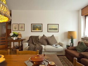 Een gezellige woonkamer met een bank, een tafeltje met theepot en kopje, een lamp en ingelijste foto's aan de muur.