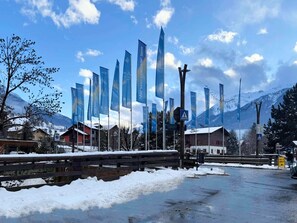 Een besneeuwd buitengebied met verschillende blauwe vlaggen, een houten omheining en gebouwen op de achtergrond.