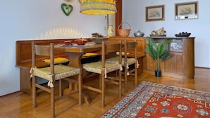 Uma sala de jantar com uma mesa de madeira, cadeiras, um candeeiro pendente e um tapete estampado.