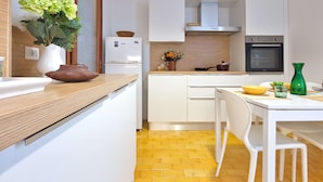 Uma cozinha compacta com armários brancos, bancada de madeira, forno embutido e piso com azulejos amarelos.