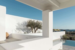Een modern terras buiten met een zwembad, witte muren en uitzicht op zee.