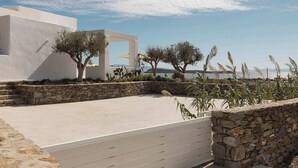 A modern outdoor area with a stone wall, a flat concrete surface, and a white building with a unique architectural design. - Golden Coast Villa Rodi Private Wadingpool Gem in Paros (Paros)