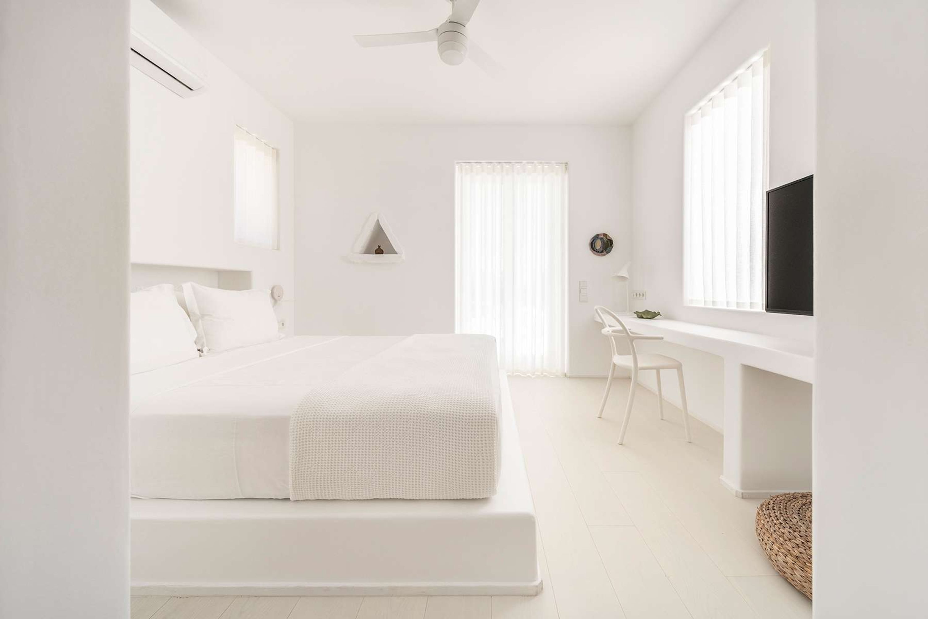Un dormitorio minimalista con cama, escritorio y televisor.