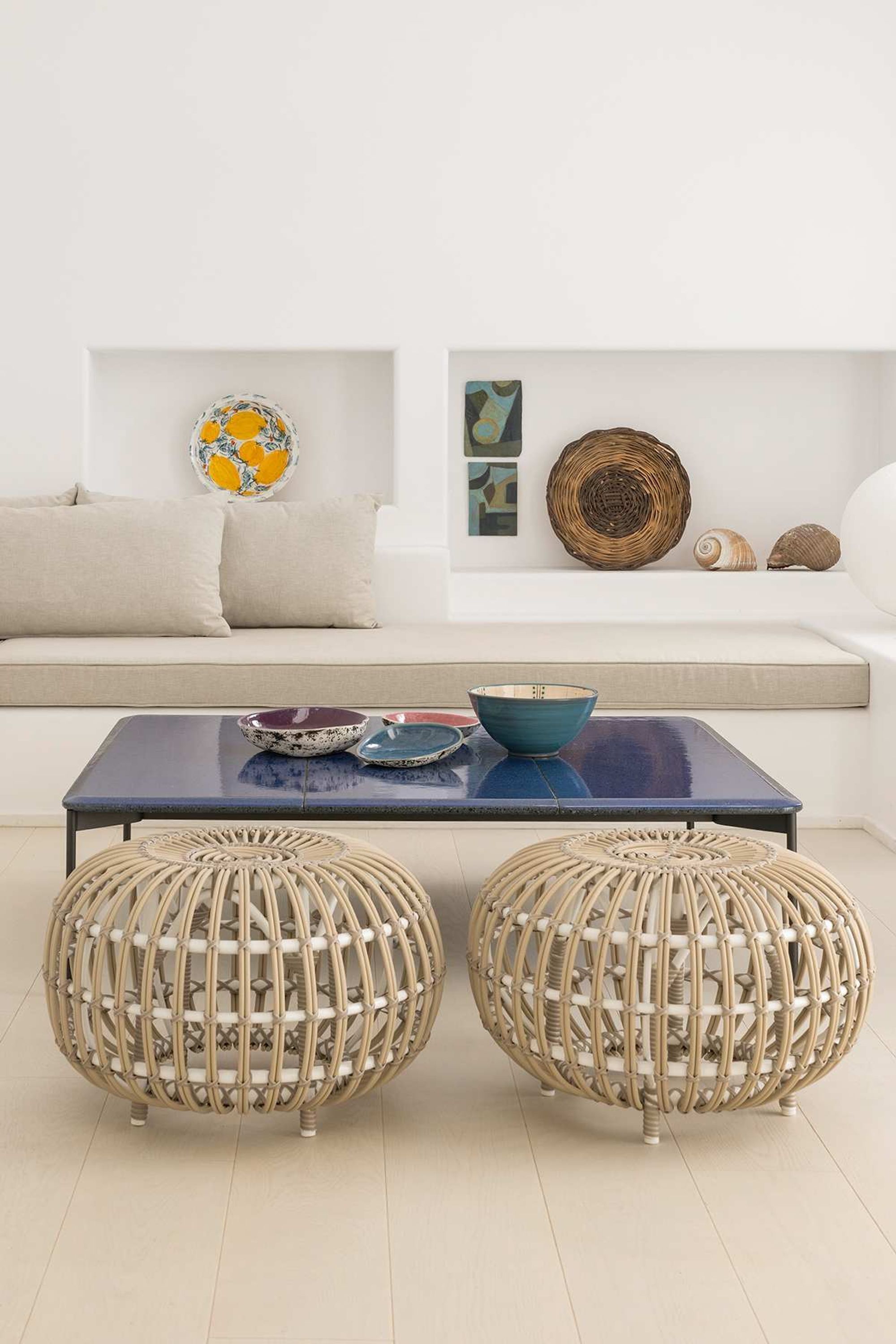 A modern living room with a sofa, a coffee table, two woven poufs, decorative wall art, and a bowl.