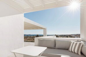 Ein moderner Außenbereich zum Verweilen mit einem weißen Tisch und einer Couch, einer Pergola und freiem Blick auf die Landschaft und das Meer.
