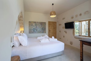A bedroom with a bed, white towels, a wooden door, a TV on the wall, and a window. - Aerida Guesthouse Of Stone - Maria Cozy Suite (Rethymno)