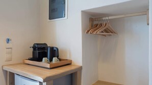 Une petite cuisine équipée d’une machine à café, de deux tasses et d’un mini-réfrigérateur. On y trouve une étagère en bois avec des cintres et un tiroir en dessous.