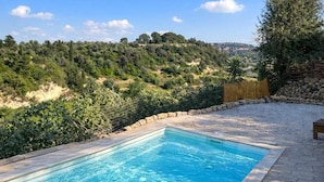 Une piscine rectangulaire à l’eau d’un bleu limpide, entourée d’une terrasse en pierre et offrant une vue sur un paysage vallonné parsemé d’arbres et d’arbustes.