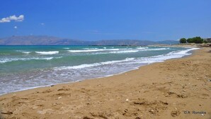 Une plage avec une eau d’un bleu limpide, un rivage sablonneux et des montagnes à l’horizon.