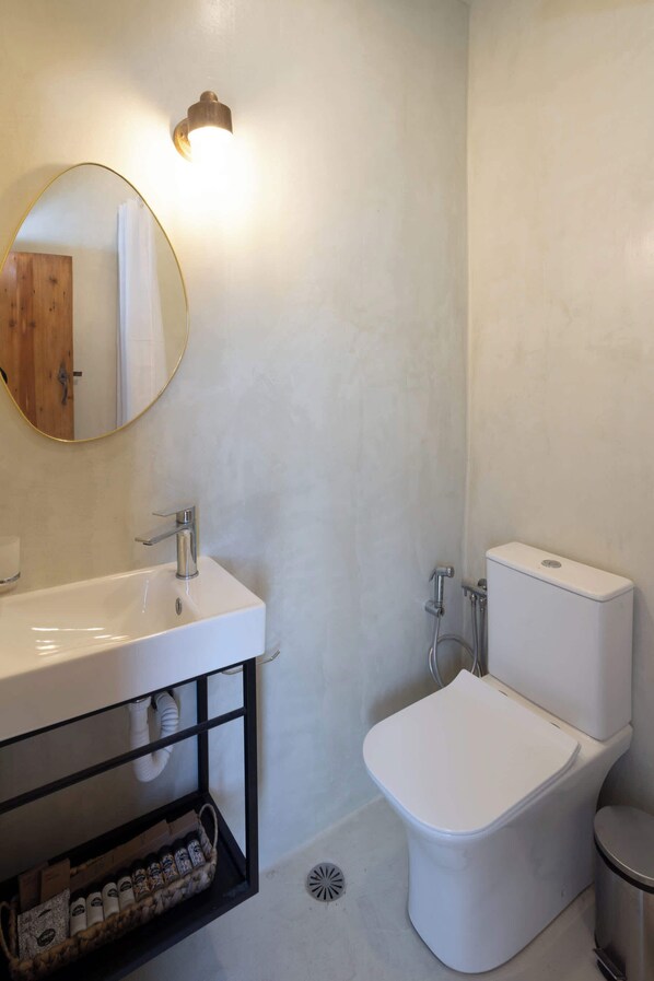 Un baño con lavamanos blanco, un espejo redondo, inodoro y ducha.