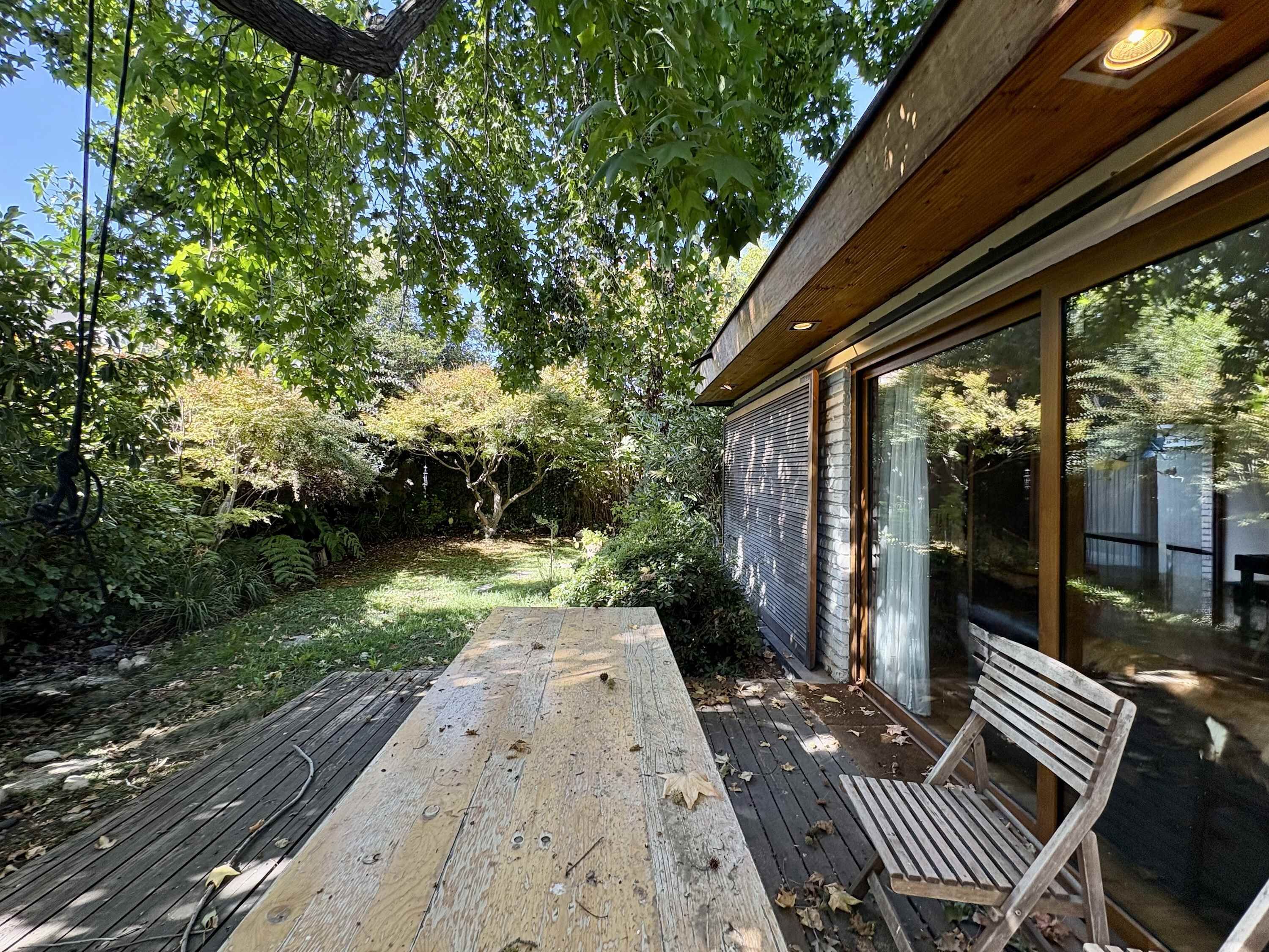 A wooden deck with a bench, surrounded by lush greenery and a tree.