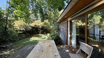 A wooden deck with a bench, surrounded by lush greenery and a tree.