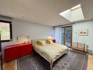 A bedroom with a skylight, a bed with multiple pillows, a red dresser, a bedside table with lamps, and a view of the outdoors through a window. - House Pedro de Valdivia Norte - Garden & Parking (Las Condes)
