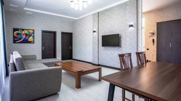 Una sala moderna con un sofá gris, una mesa de centro de madera, una mesa de comedor con sillas, un televisor montado en la pared y una puerta con un teléfono en la pared.